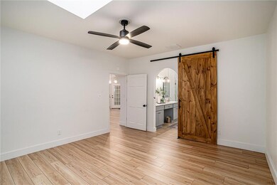 Empty room featuring a ceiling fan, light wood finished floors, a barn door, and a skylight