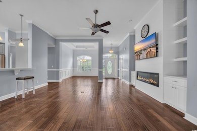 Unfurnished living room with dark wood-style flooring, ornamental molding, a glass covered fireplace, ceiling fan, and built in features