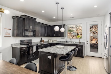 Kitchen with black appliances, light stone countertops, hanging light fixtures, a kitchen breakfast bar, and light wood finished floors
