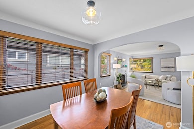 Bright dining area with rich hardwood floors and classic arched entryway opening to cozy living room. Large windows bring in abundant natural light