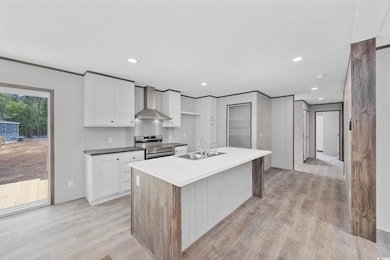 Kitchen featuring wall chimney range hood, a sink, electric stove, light wood-type flooring, and white cabinetry