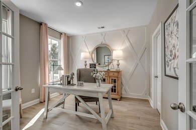 Office space featuring light wood-type flooring, visible vents, baseboards, and a decorative wall