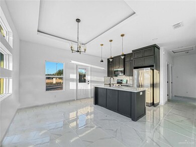 Kitchen featuring pendant lighting, a raised ceiling, a center island with sink, and appliances with stainless steel finishes