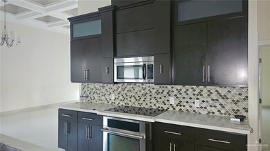 Kitchen with backsplash, appliances with stainless steel finishes, hanging light fixtures, light stone counters, and coffered ceiling