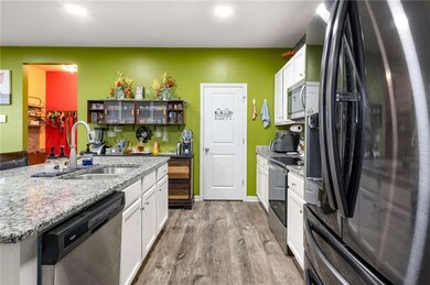 Kitchen with stainless steel appliances, wood finished floors, white cabinets, a sink, and an island with sink