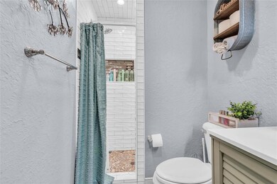 Full bathroom featuring a textured wall, a tile shower, and vanity