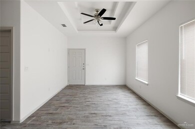 Empty room with a tray ceiling, wood finish floors, and a ceiling fan
