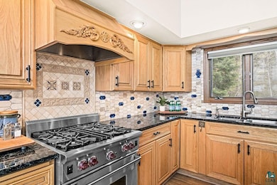 Kitchen with high end stainless steel range oven, a sink, backsplash, and dark stone counters