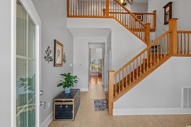 Tiled entryway with stairway, baseboards, a chandelier, a towering ceiling, and visible vents