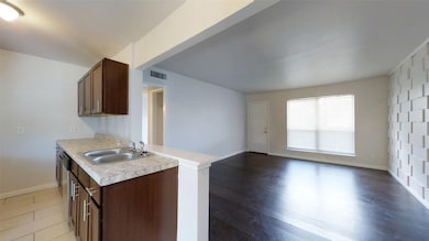 Kitchen with dark brown cabinets, light countertops, open floor plan, light wood-style floors, and stainless steel dishwasher