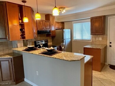 Kitchen with backsplash, brown cabinets, light tile patterned floors, light stone counters, and a peninsula