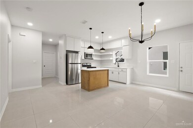 Kitchen with a center island, stainless steel appliances, light countertops, hanging light fixtures, and white cabinetry