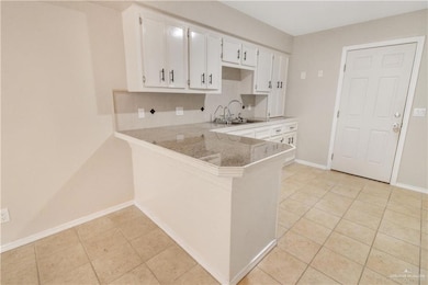 Kitchen featuring light tile patterned flooring, white cabinets, a peninsula, and tile counters