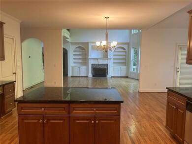 Kitchen featuring wood finished floors, arched walkways, open floor plan, built in shelves, and a chandelier