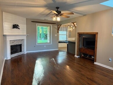 Unfurnished living room with ceiling fan, a stone fireplace, and dark wood-type flooring
