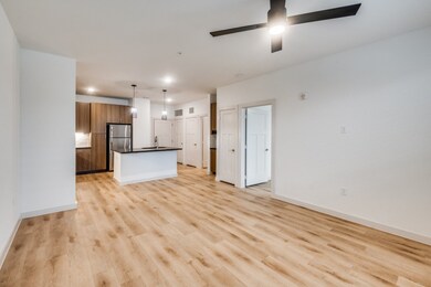 Kitchen with dark countertops, light wood-style flooring, brown cabinets, a center island with sink, and decorative light fixtures