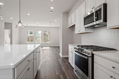 Kitchen with appliances with stainless steel finishes, light countertops, tasteful backsplash, dark wood-style flooring, and white cabinetry