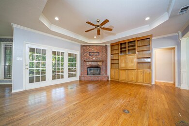Unfurnished living room with a tray ceiling, a ceiling fan, crown molding, light wood-type flooring, and a fireplace