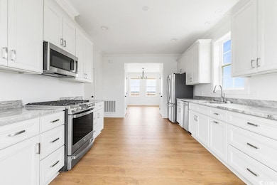 Kitchen with appliances with stainless steel finishes, a sink, a chandelier, plenty of natural light, and ornamental molding
