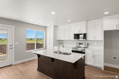 Kitchen featuring white cabinetry, stainless steel appliances, a center island with sink, a breakfast bar, and wood finished floors