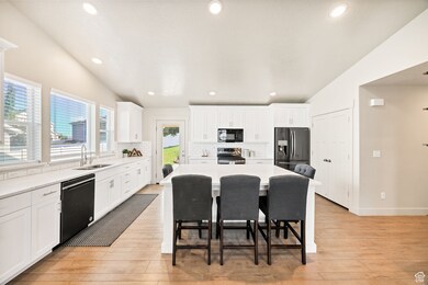 Kitchen with black appliances, a kitchen bar, light wood-type flooring, white cabinets, and recessed lighting