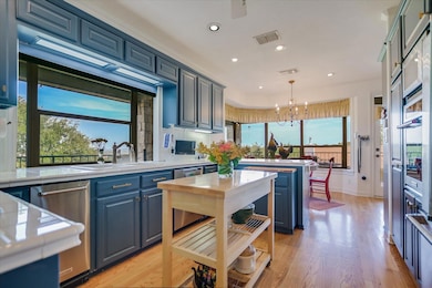 Kitchen with blue cabinets, a chandelier, light wood-style flooring, recessed lighting, and tile countertops