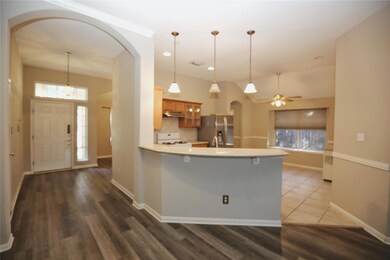 Kitchen featuring arched walkways, glass insert cabinets, light countertops, stainless steel fridge, and pendant lighting