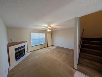 Unfurnished living room with a fireplace, stairway, light carpet, a textured ceiling, and a ceiling fan