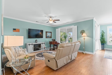 Living area featuring light wood-style floors, crown molding, healthy amount of natural light, and a glass covered fireplace