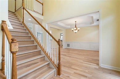 Stairway with a chandelier, a raised ceiling, and wood finished floors