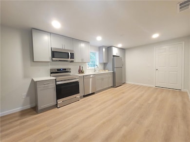 Kitchen featuring appliances with stainless steel finishes, gray cabinets, light countertops, light wood-type flooring, and recessed lighting