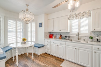 Kitchen with light stone countertops, tasteful backsplash, light wood finished floors, white cabinets, and a ceiling fan