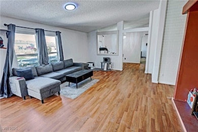 Living room featuring a textured ceiling, light wood-style floors, and lofted ceiling