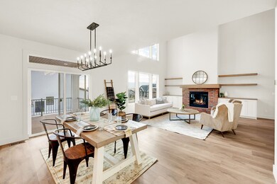 Dining area featuring a brick fireplace, light wood-style floors, a chandelier, and a high ceiling