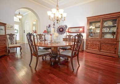 Dining area with a chandelier, arched walkways, ornamental molding, and wood finished floors
