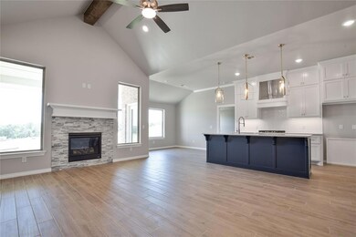 Kitchen with a fireplace, an island with sink, beamed ceiling, pendant lighting, and high vaulted ceiling