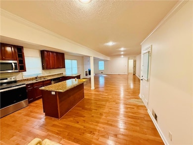 Kitchen featuring appliances with stainless steel finishes, a center island, a textured ceiling, ornamental molding, and light stone countertops