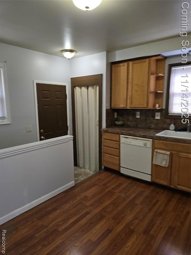 Kitchen with dark wood-style flooring, dark countertops, tasteful backsplash, dishwashing machine, and brown cabinetry