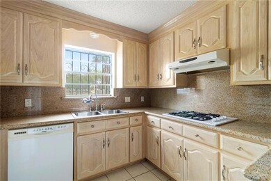 Kitchen with a textured ceiling, white appliances, light brown cabinets, and sink