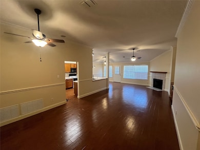 Unfurnished living room with a ceiling fan, ornamental molding, a tiled fireplace, and dark wood-style floors