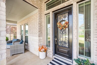 This home features a welcoming front porch with comfortable seating, a decorative glass and iron front door, and tasteful brick and stone accents. Perfect for relaxing outdoors.