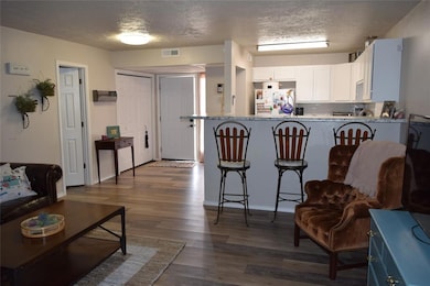 Kitchen featuring freestanding refrigerator, white cabinetry, dark wood-type flooring, a kitchen breakfast bar, and a textured ceiling
