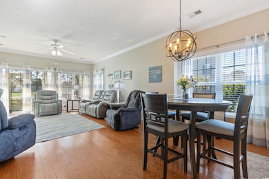 Dining area featuring ceiling fan, wood finished floors, a chandelier, ornamental molding, and a textured ceiling