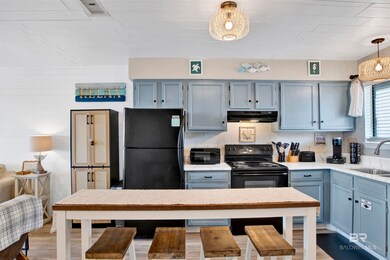 Kitchen featuring a sink, under cabinet range hood, light countertops, pendant lighting, and blue cabinets