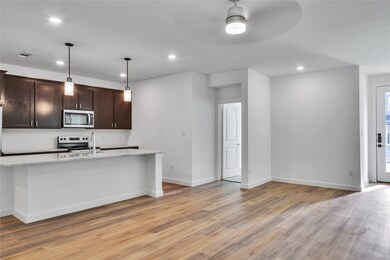 Kitchen featuring stainless steel appliances, dark brown cabinetry, light wood-style floors, and light stone counters