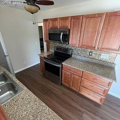 Kitchen with appliances with stainless steel finishes, ceiling fan, tasteful backsplash, dark wood-style floors, and stone counters