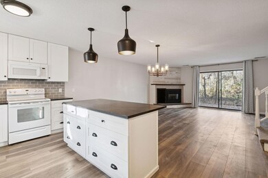 Bright, open-concept main level featuring a spacious kitchen with center island, stylish lighting, and a cozy fireplace overlooking the private wooded backdrop.