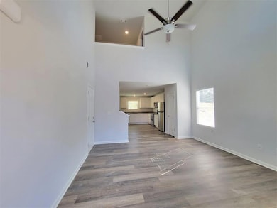 Unfurnished living room featuring ceiling fan, a high ceiling, and light wood-type flooring