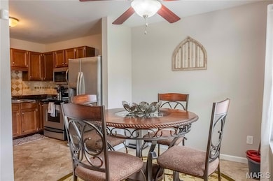 Kitchen featuring dark countertops, brown cabinets, decorative backsplash, appliances with stainless steel finishes, and ceiling fan