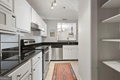 Kitchen with stainless steel appliances, a sink, a notable chandelier, white cabinetry, and under cabinet range hood
